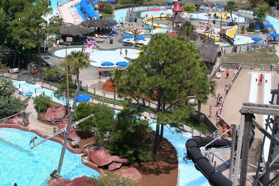 A water park with multiple pools, slides, and a large tree in the foreground.