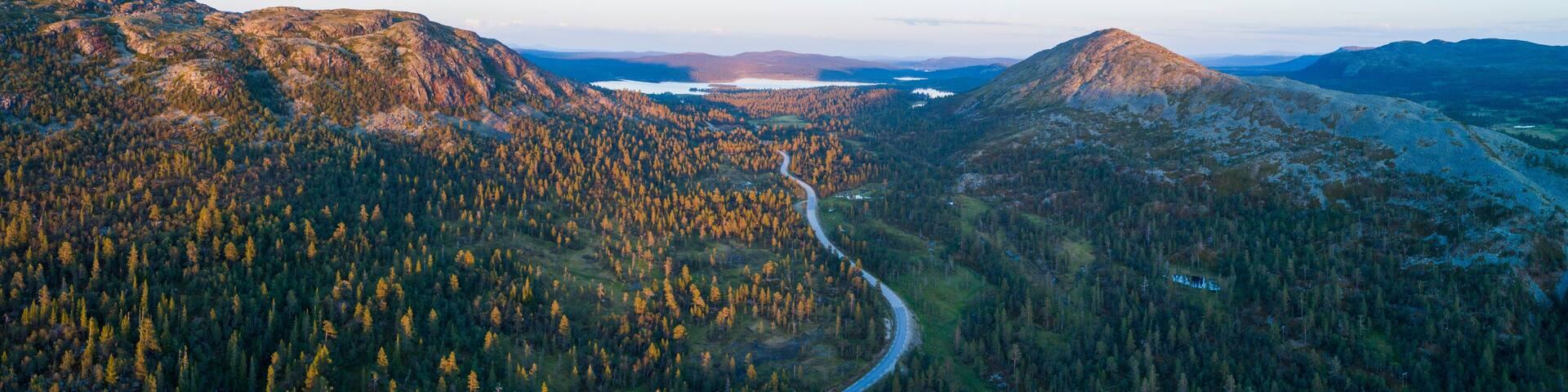 High angle aerial view of oad running through forest and mountainous landscape in northern Sweden