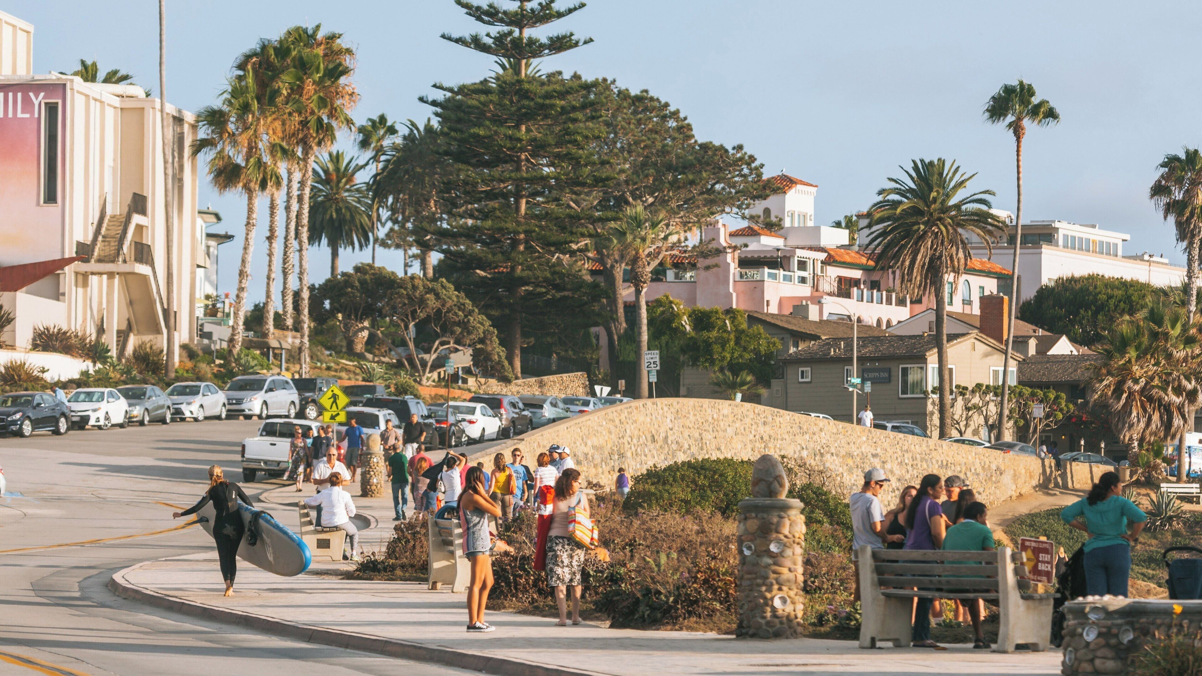 Experience the vibrant atmosphere at La Jolla Cove with surfers, beachgoers, and stunning coastal views in sunny California