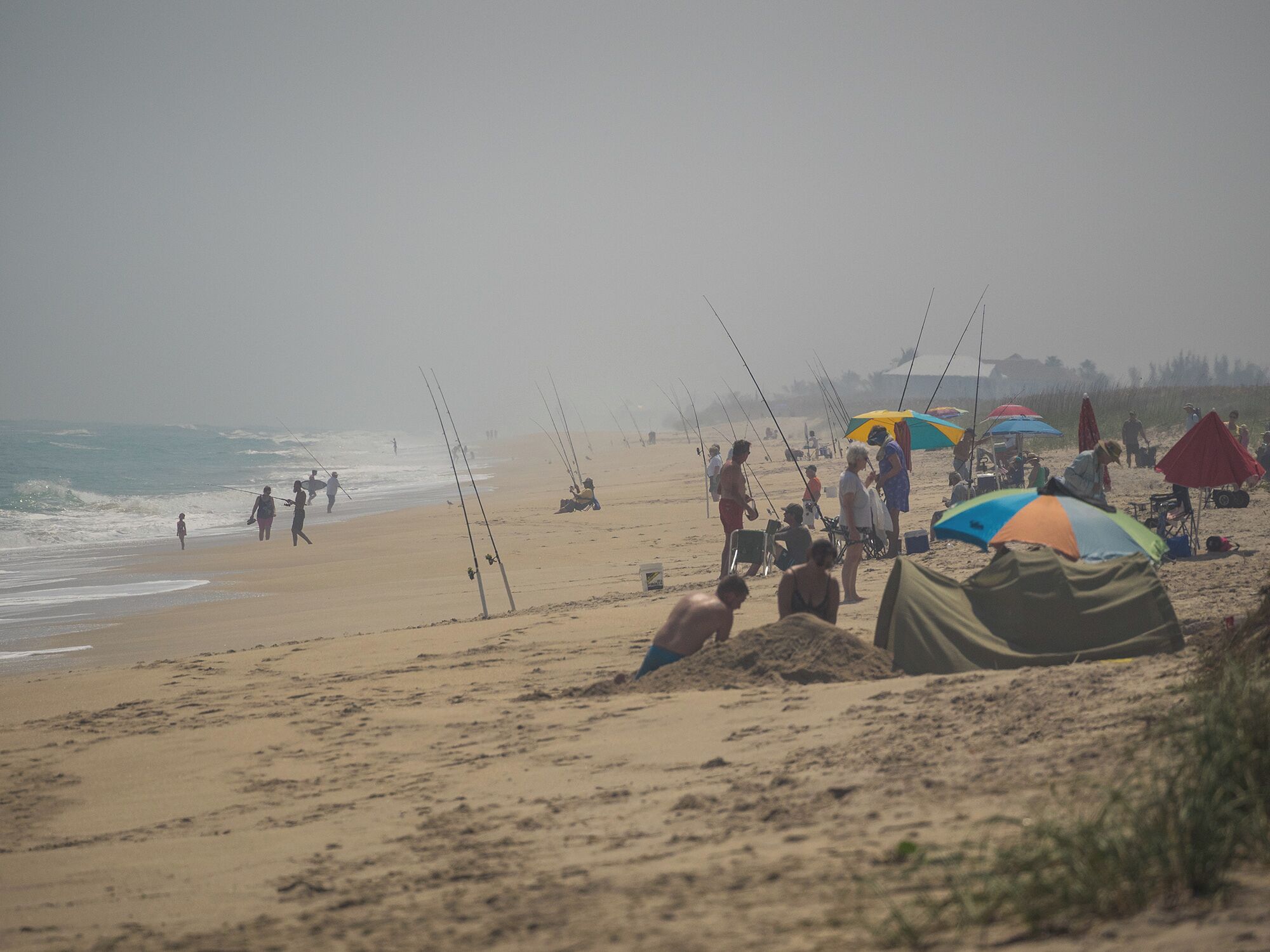 A beach with people fishing and tents set up.