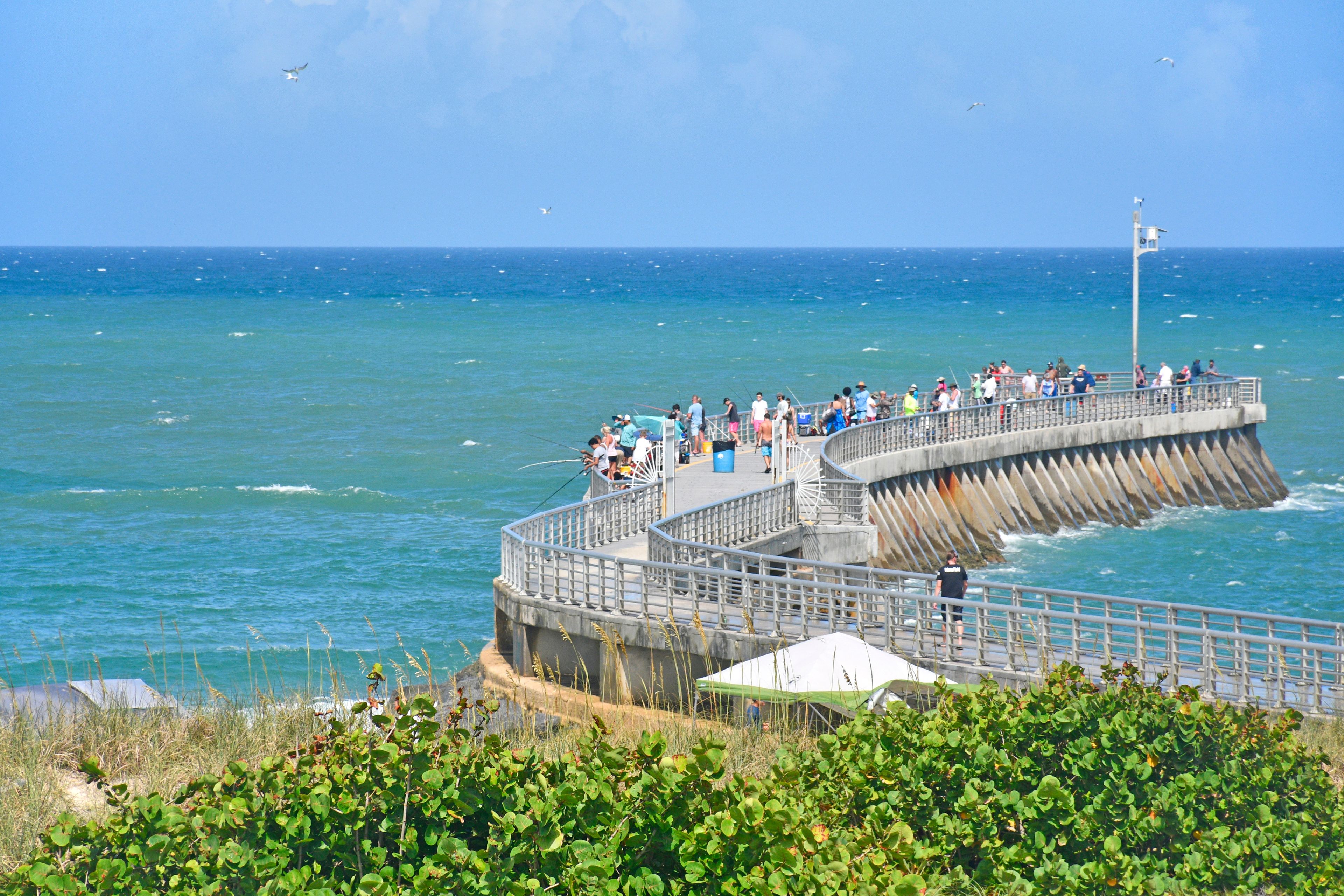 Un muelle con gente pescando, un faro y el océano.