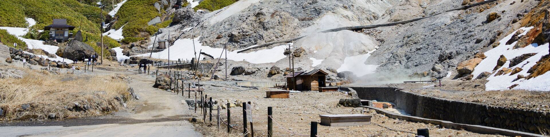 A mountainous landscape with a small wooden structure, a dirt path, and a rocky terrain with patches of snow.