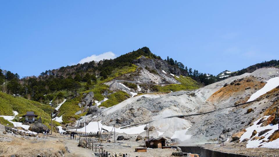 A mountainous landscape with a small wooden structure, a dirt path, and a rocky terrain with patches of snow.