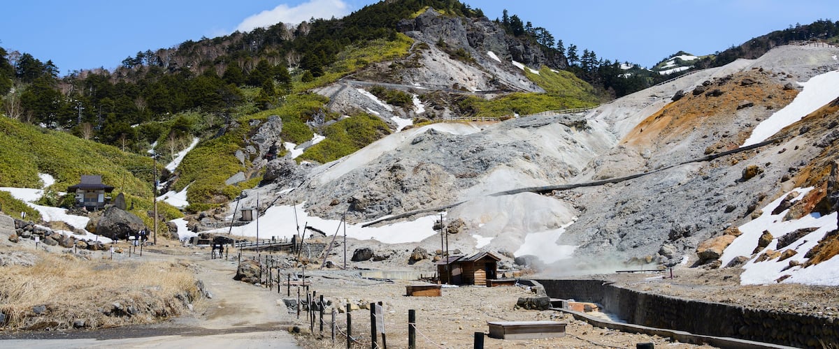 A mountainous landscape with a small wooden structure, a dirt path, and a rocky terrain with patches of snow.