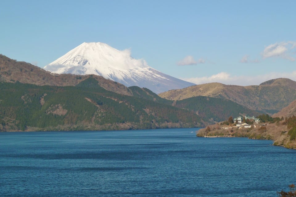 A snow-capped mountain, a lake, and a building on a hillside.