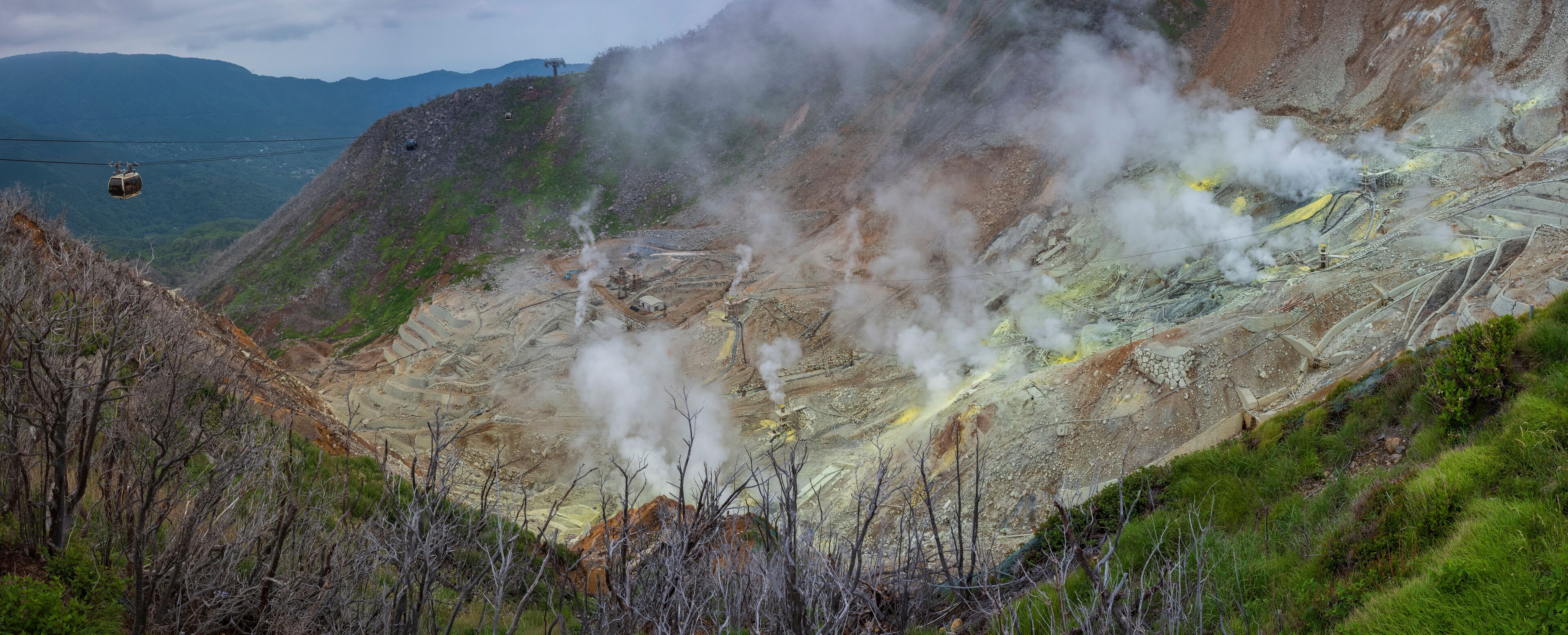 A mountainous landscape with a cable car, steam vents, and terraced mining areas.