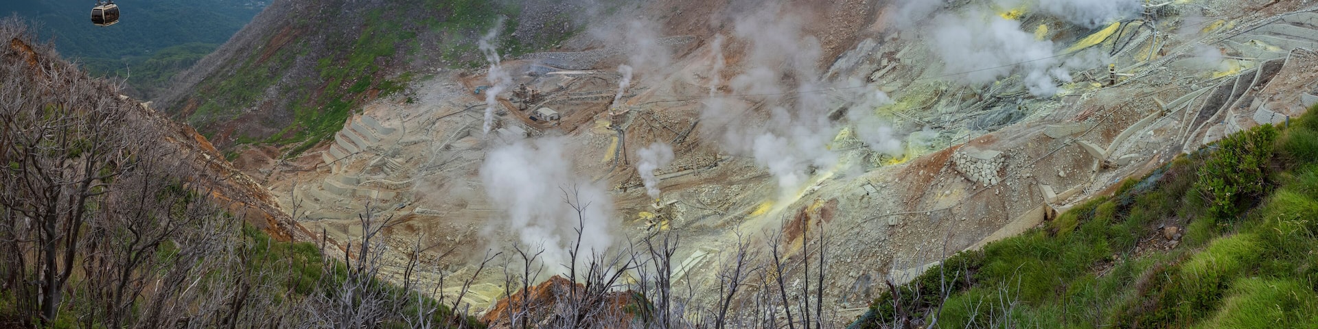 A mountainous landscape with a cable car, steam vents, and terraced mining areas.