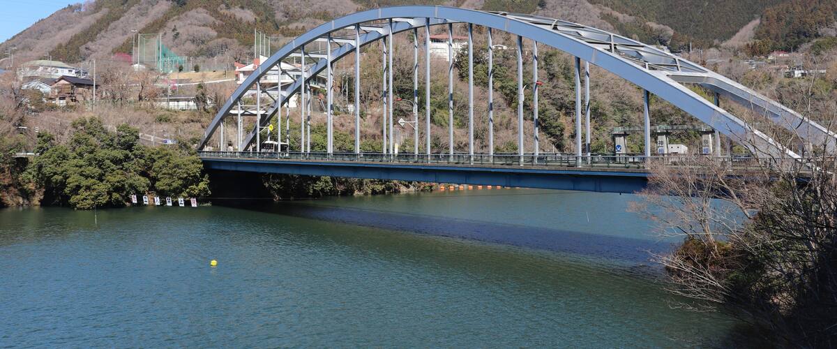 A steel arch bridge over a river with hills in the background.