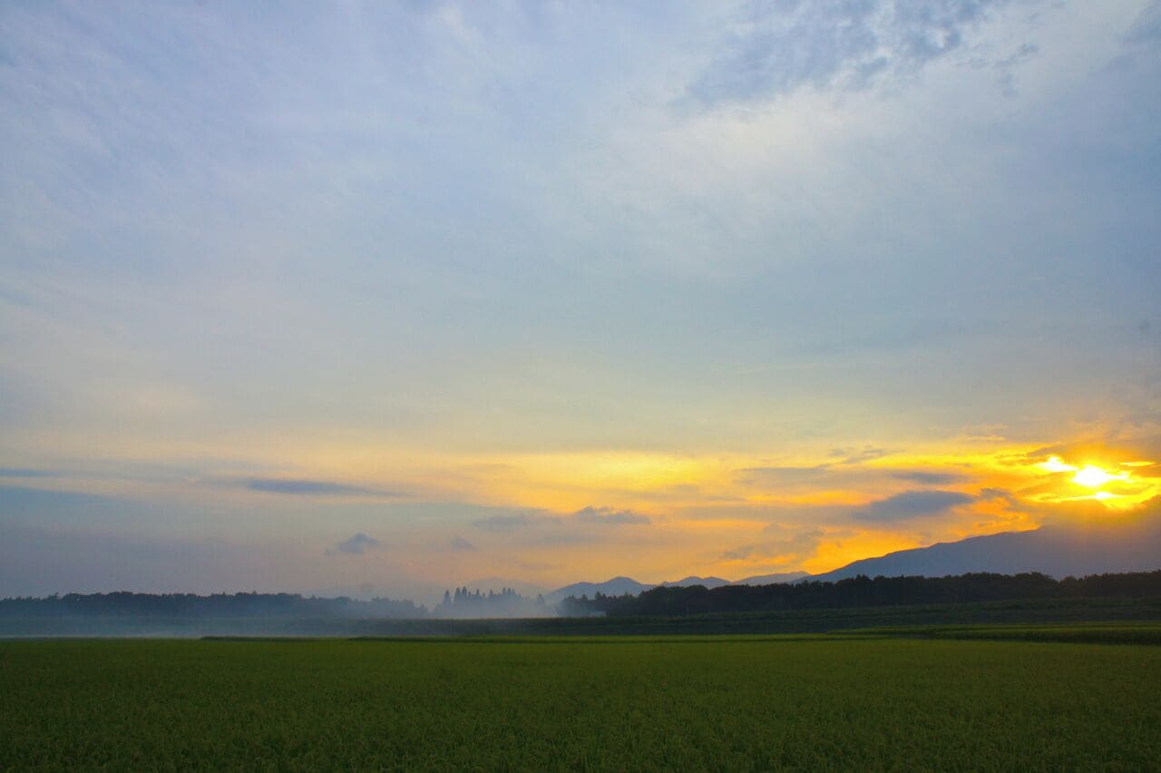 A sunset over a green field with distant mountains.
