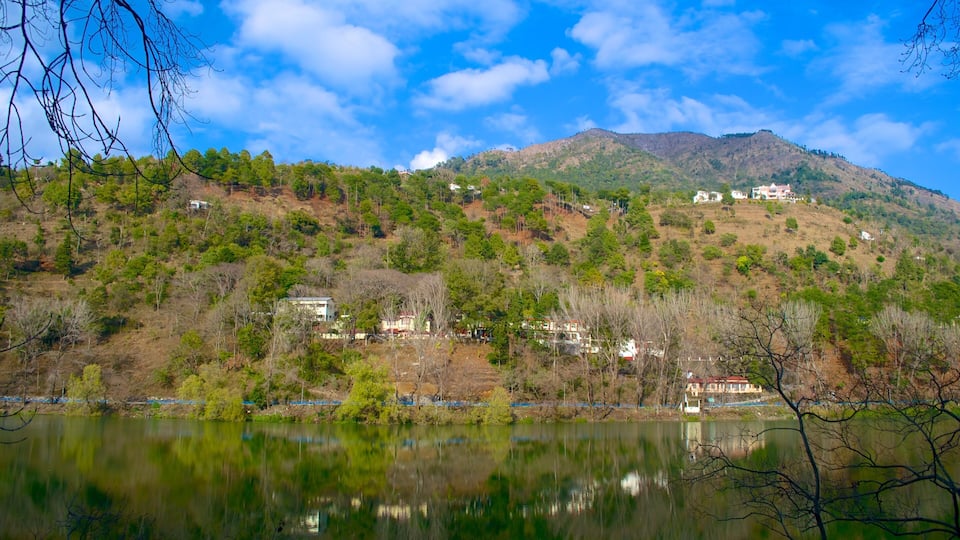 A lake with reflections, a hill with scattered buildings, and a clear blue sky.