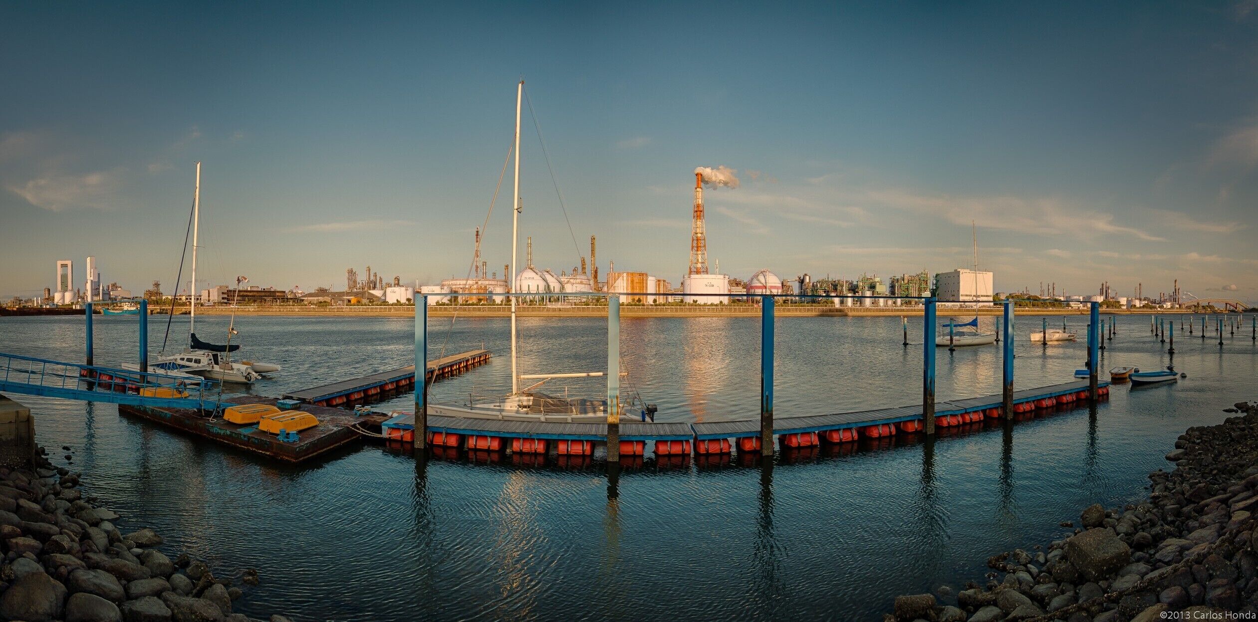 A harbor with boats, a dock, and industrial buildings in the background.
