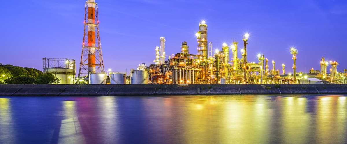 An industrial complex with multiple tall structures and tanks, reflecting on the water surface.
