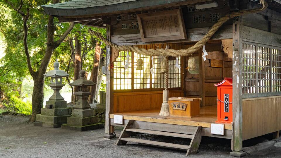 A traditional Japanese shrine with a wooden structure, stone lanterns, and a red box.