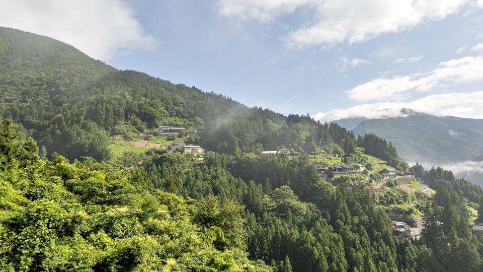 A mountainous landscape with dense forests and several buildings nestled among the hills.