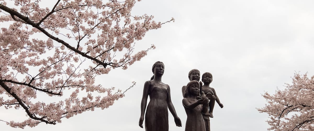 A statue of a woman holding a child, surrounded by cherry blossoms.
