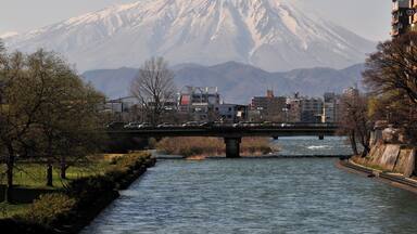 A river with a bridge, a snow-capped mountain, and buildings in the foreground.