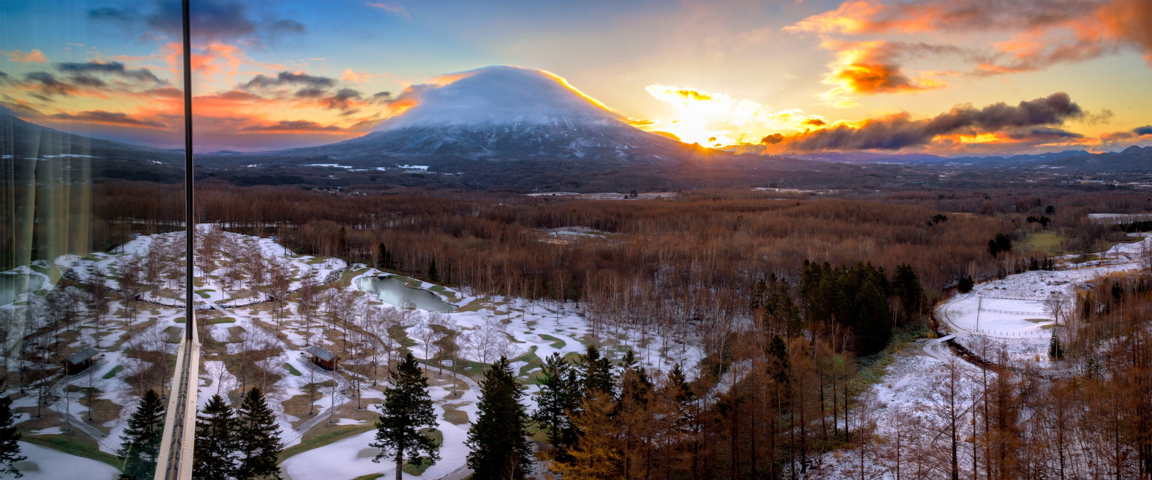 A snowy landscape with a mountain in the background and a sunset.