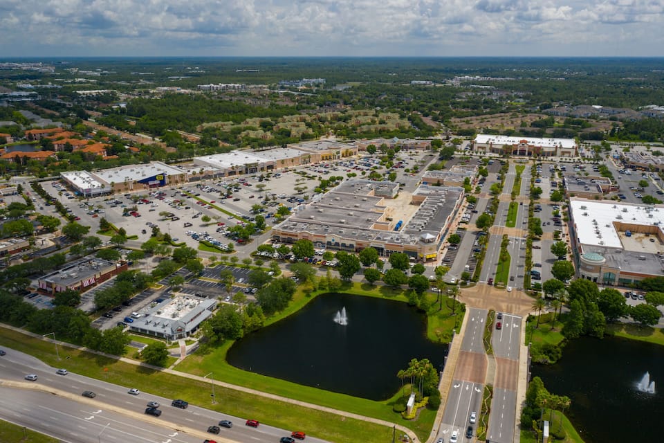 An aerial view of a commercial area with parking lots, a large building, and a lake with fountains.