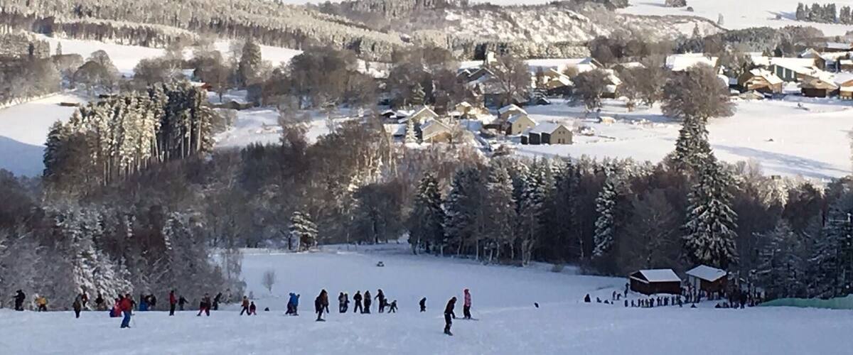 A snowy landscape with a ski resort, trees, and distant hills.
