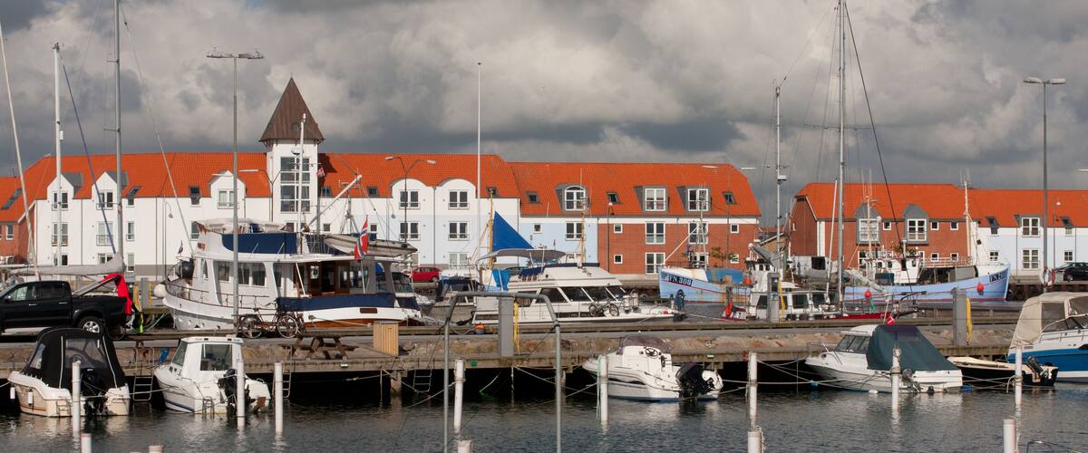 A marina with boats docked, a red-roofed building, and cloudy skies.