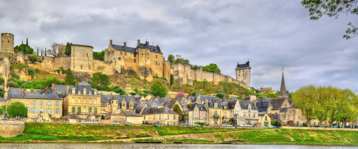 A historic castle on a hill overlooking a river, surrounded by traditional buildings.