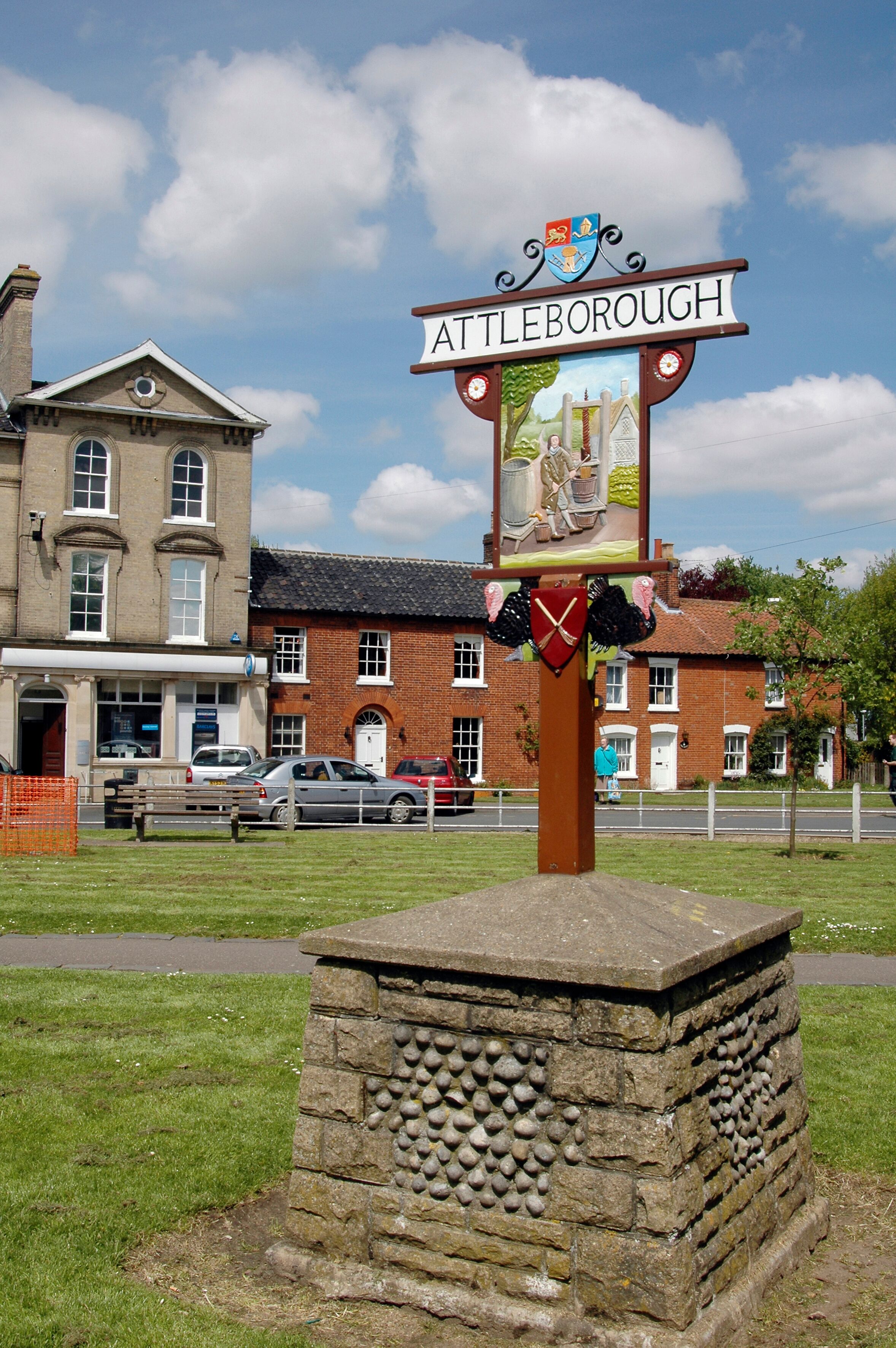 A signpost with 'Attleborough' written on it, a stone structure, and a building in the background.