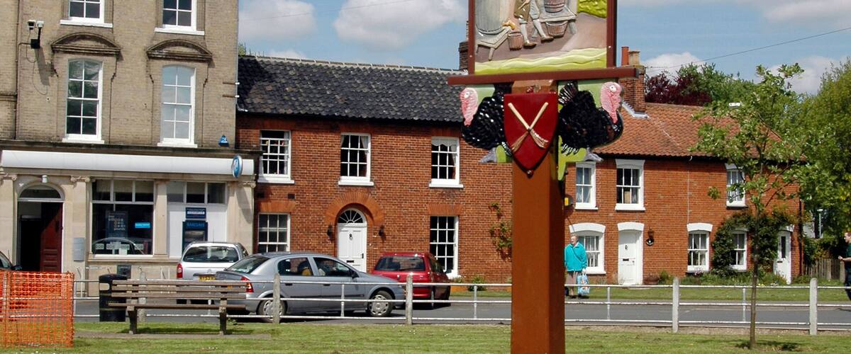 A signpost with 'Attleborough' written on it, a stone structure, and a building in the background.