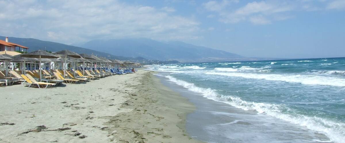 A beach with rows of sun loungers and umbrellas, a sandy shore, and waves crashing onto the beach.