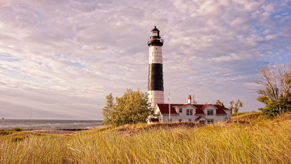 A lighthouse, a white house with a red roof, and a beach in the background.