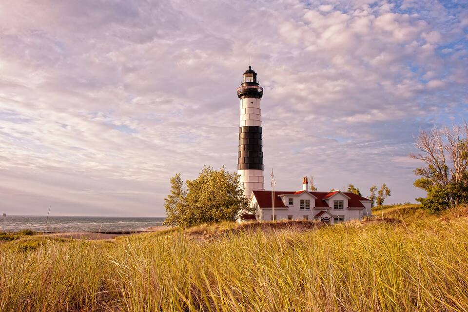 Un phare, une maison blanche avec un toit rouge, et une plage en arrière-plan.