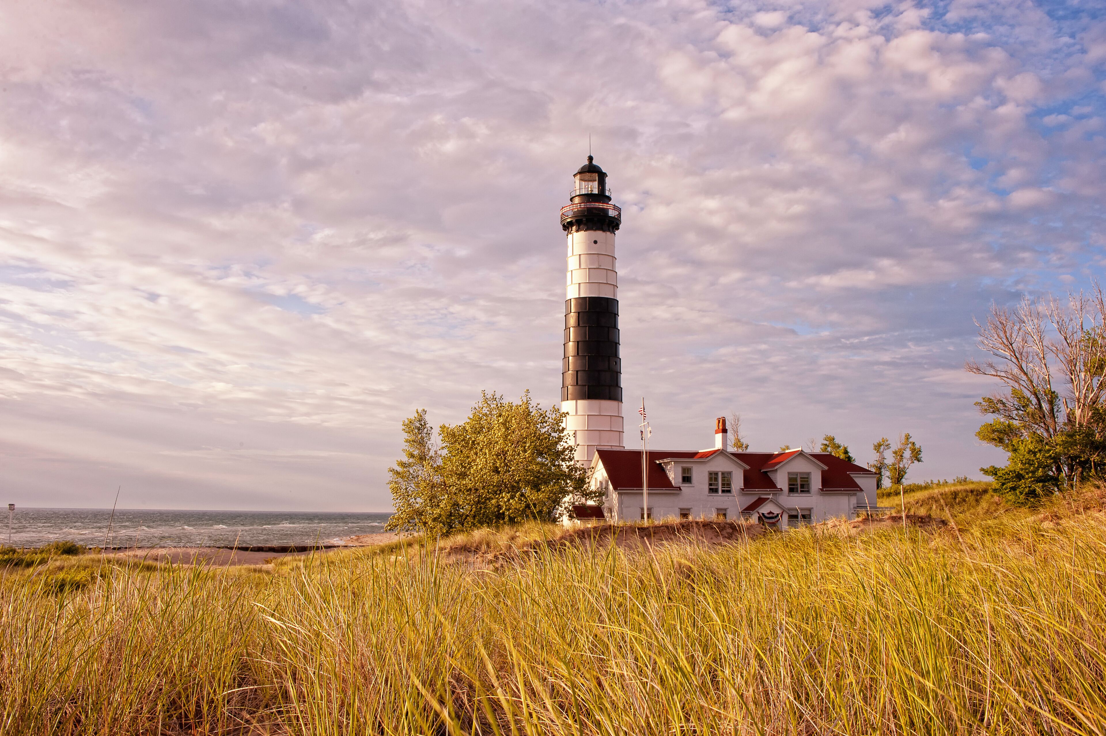 A lighthouse, a white house with a red roof, and a beach in the background.