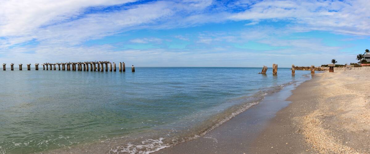 A beach with a row of wooden posts extending into the water, a sandy shore, and a clear sky.