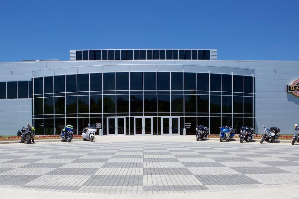 Un edificio moderno con una amplia fachada de vidrio y el logotipo de Harley-Davidson a la derecha.