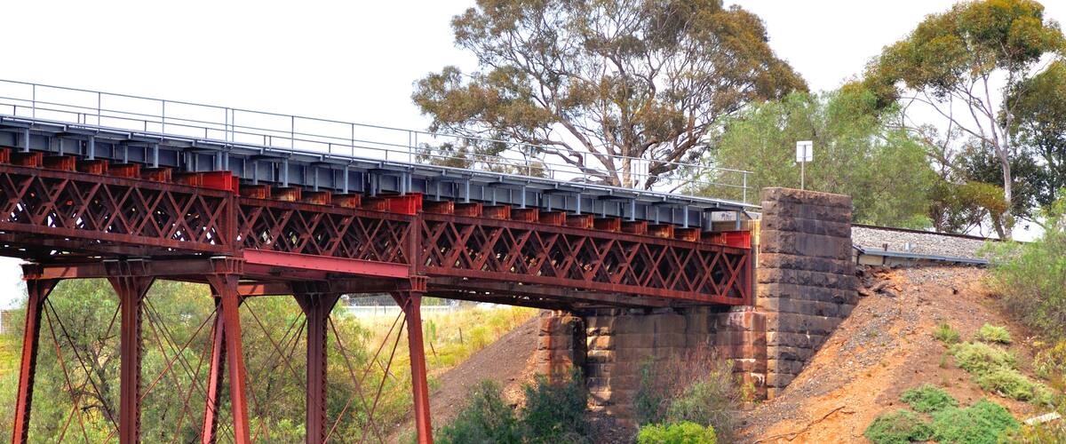 A red metal bridge over a rocky terrain with trees in the background.