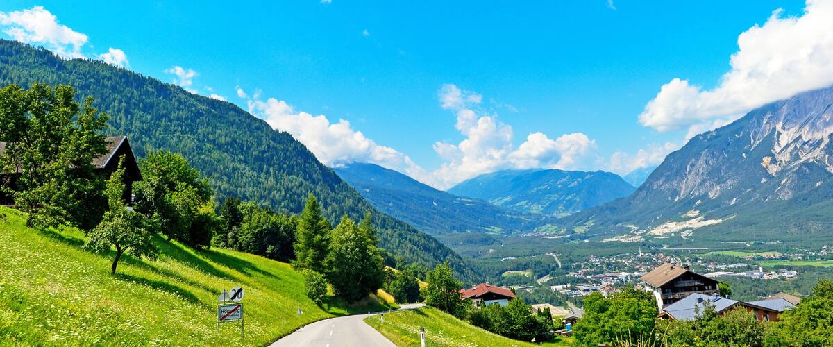 A mountain road winding through a valley with houses and a town in the distance.