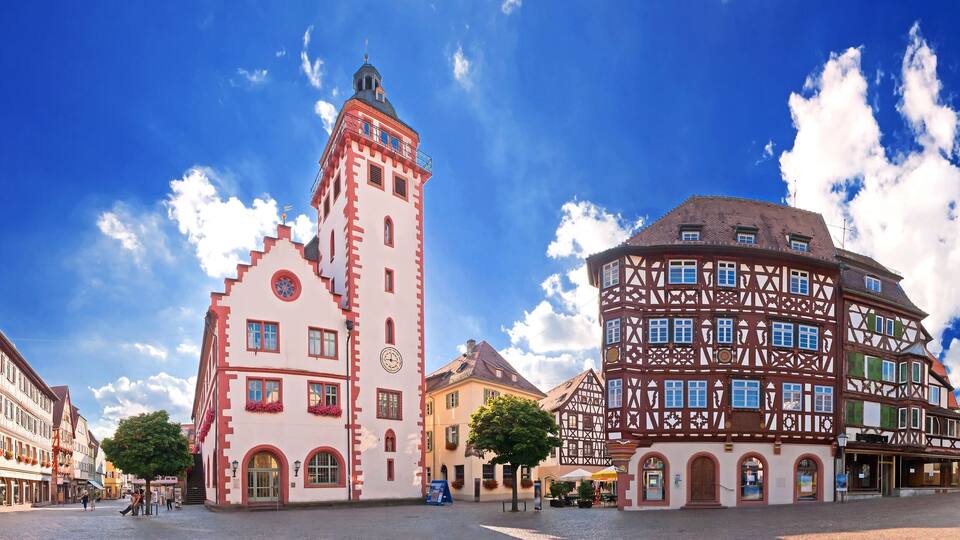 A European town square with traditional half-timbered buildings and a prominent tower.