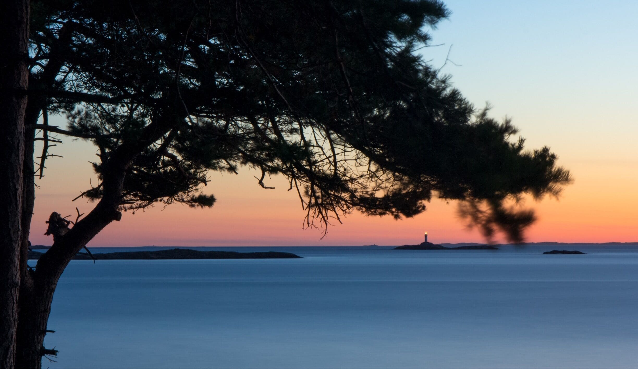 A sunset over a calm sea with a lighthouse on a small island in the distance.