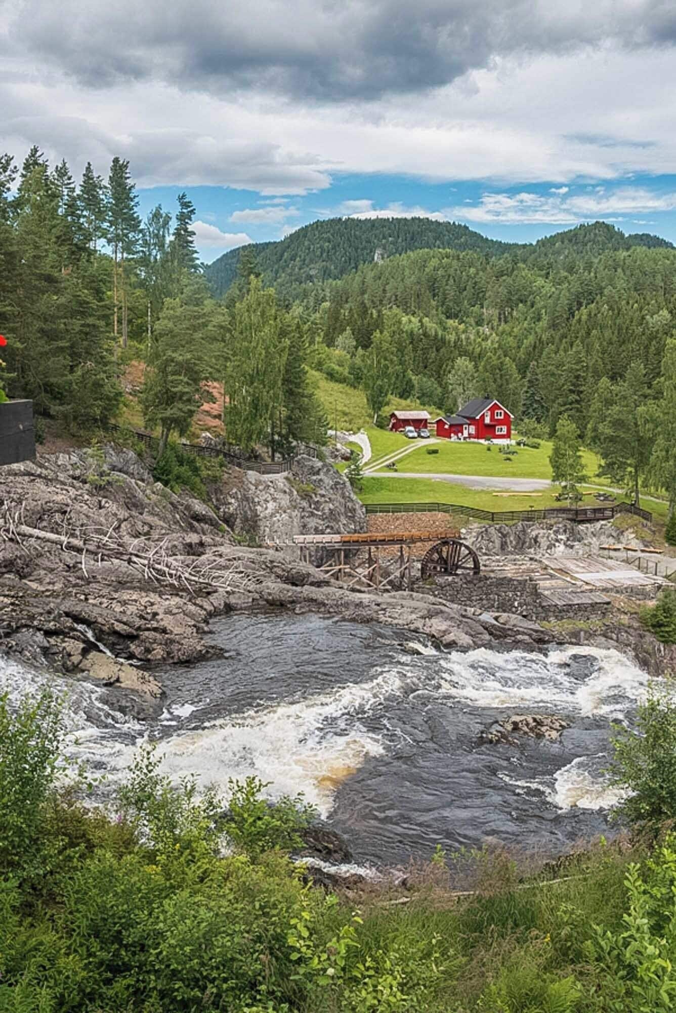 A red house on a hill, a river, and a forested mountain range.