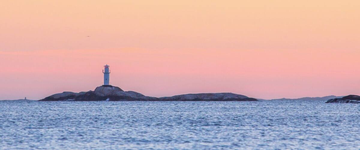 A lighthouse on a rocky outcrop surrounded by calm water.