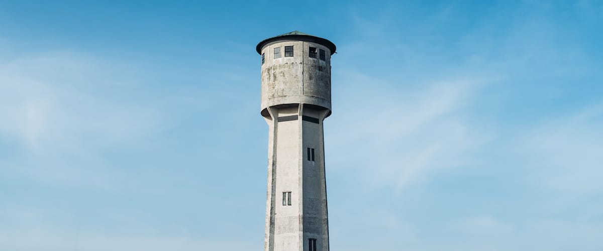 A tall, cylindrical lighthouse with a rounded top and windows, set against a clear blue sky.