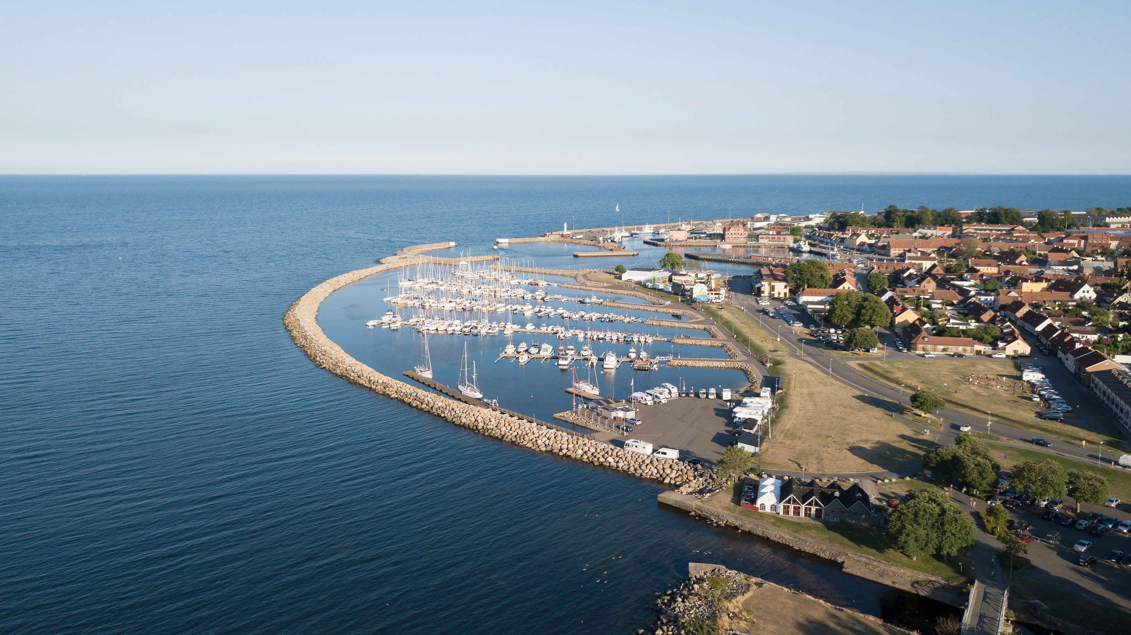 A coastal marina with boats, a breakwater, and a town with houses and a church.