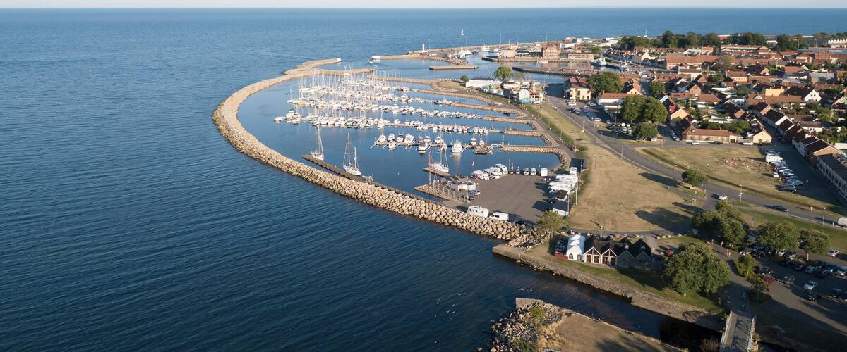 A coastal marina with boats, a breakwater, and a town with houses and a church.