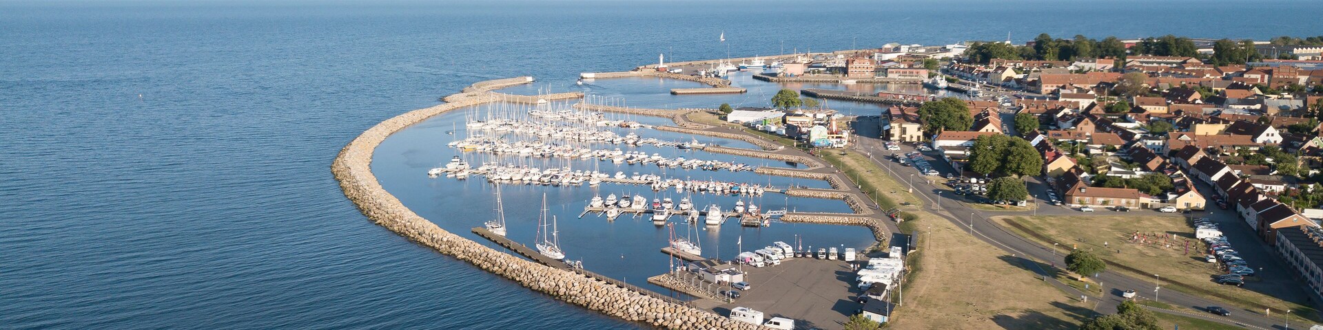 A coastal marina with boats, a breakwater, and a town with houses and a church.