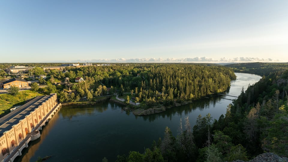 A river winding through a forested valley with a bridge and buildings in the background.