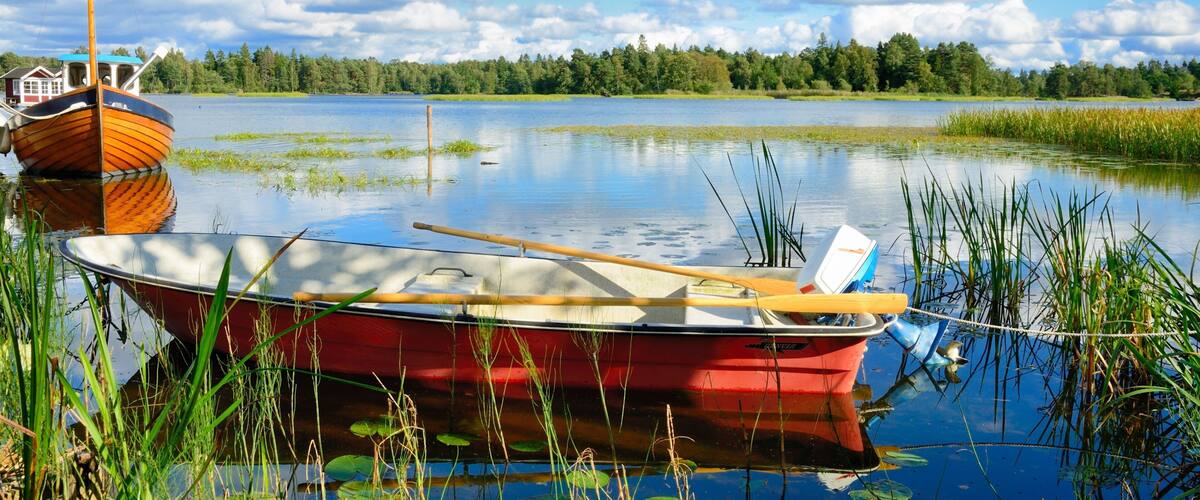 A calm lake with a red boat and a wooden boat anchored nearby.