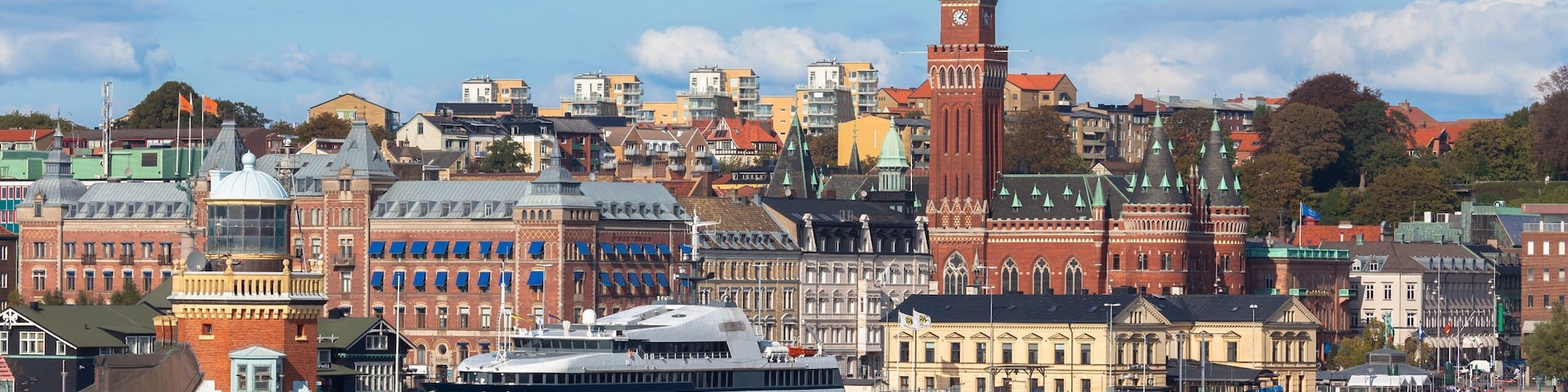 A historic cityscape with a prominent clock tower and a large ship docked at the harbor.