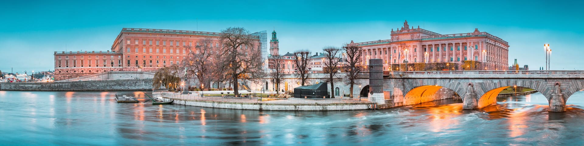 A river with a bridge, two large buildings with classical architecture, and a clock tower.