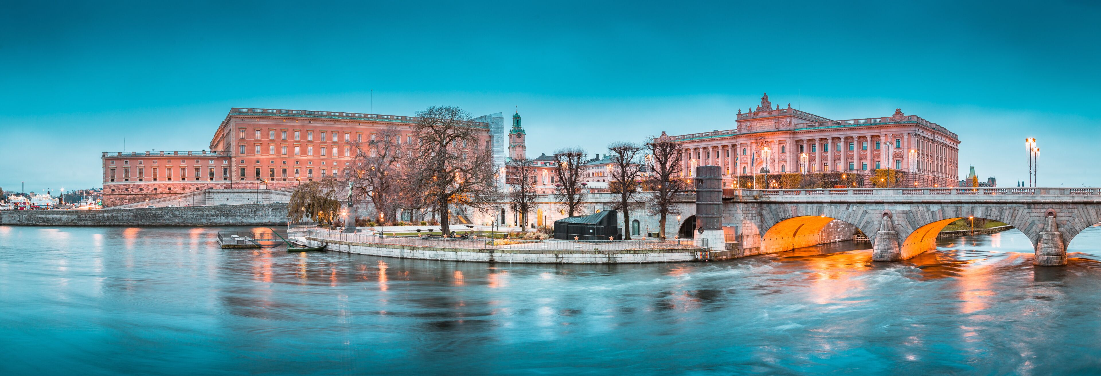 A river with a bridge, two large buildings with classical architecture, and a clock tower.