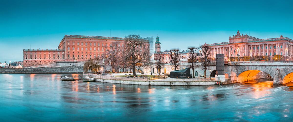 A river with a bridge, two large buildings with classical architecture, and a clock tower.