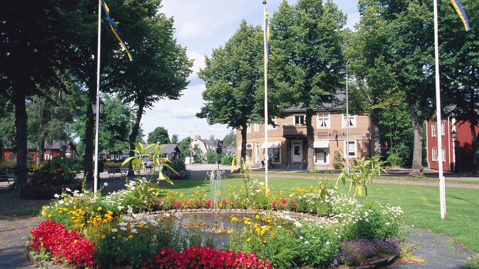 A park with a flower bed, a fountain, and a building in the background.